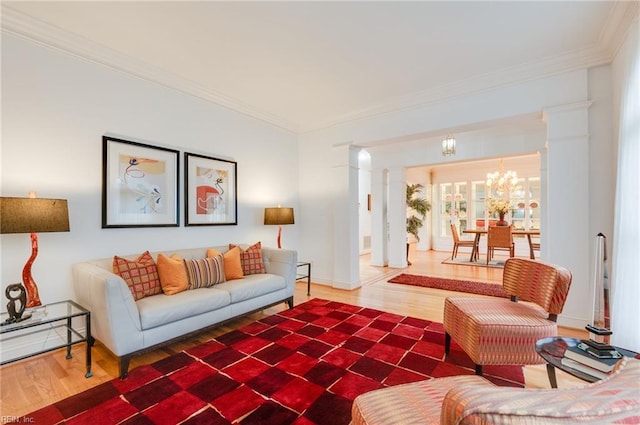 living room featuring decorative columns, ornamental molding, hardwood / wood-style floors, and a chandelier