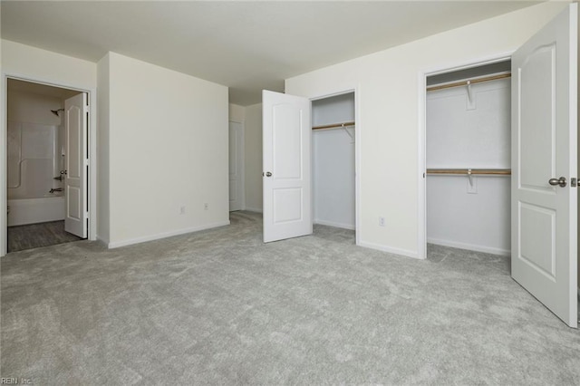 unfurnished bedroom with ensuite bath, light colored carpet, and two closets