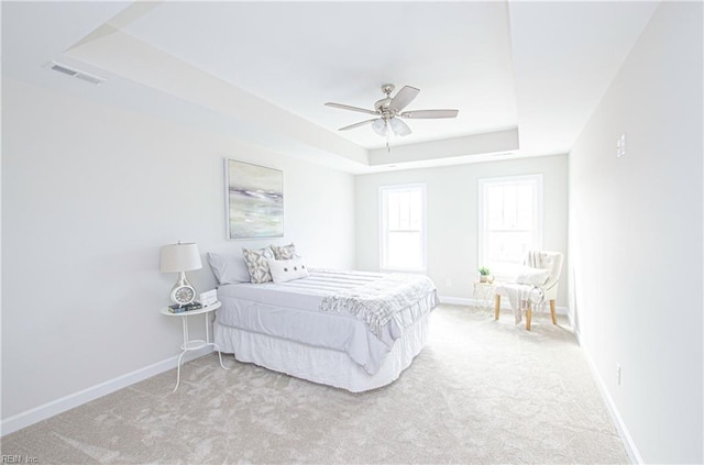 carpeted bedroom with a raised ceiling and ceiling fan