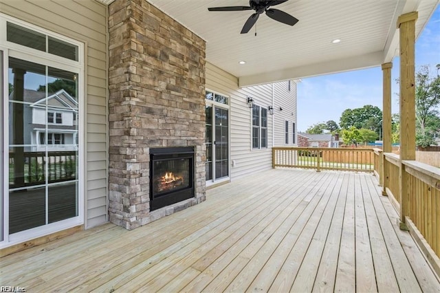 wooden deck featuring ceiling fan and an outdoor stone fireplace