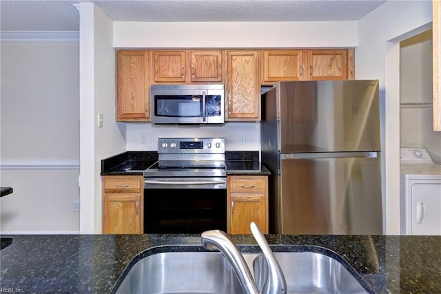 kitchen with dark stone countertops, washer / clothes dryer, sink, and appliances with stainless steel finishes