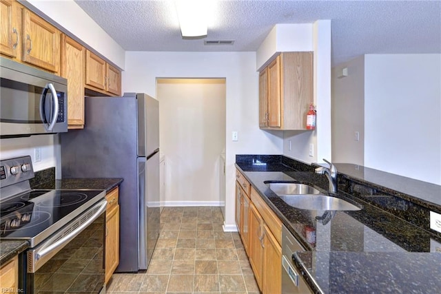 kitchen featuring sink, stainless steel appliances, dark stone counters, and a textured ceiling