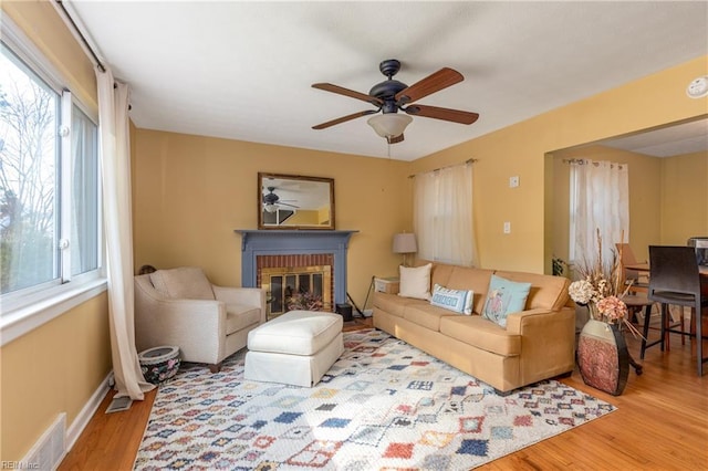 living room featuring a brick fireplace, wood-type flooring, and ceiling fan