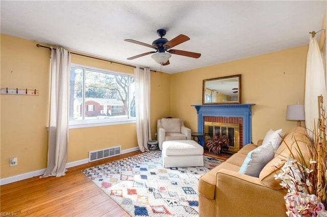 living area featuring ceiling fan, a brick fireplace, and light hardwood / wood-style floors