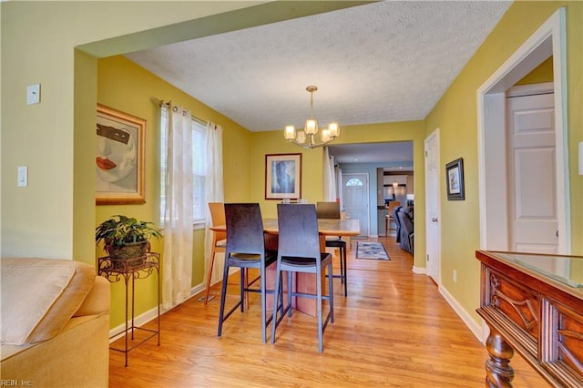 dining area featuring a textured ceiling, light hardwood / wood-style flooring, and a chandelier