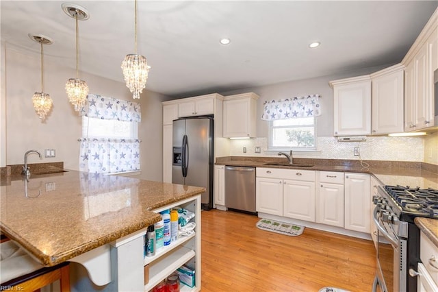 kitchen featuring appliances with stainless steel finishes, sink, white cabinets, dark stone counters, and hanging light fixtures