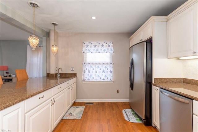 kitchen with white cabinetry, decorative light fixtures, stainless steel appliances, and dark stone counters