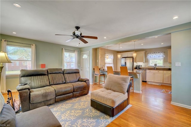 living room with ceiling fan, sink, and light wood-type flooring