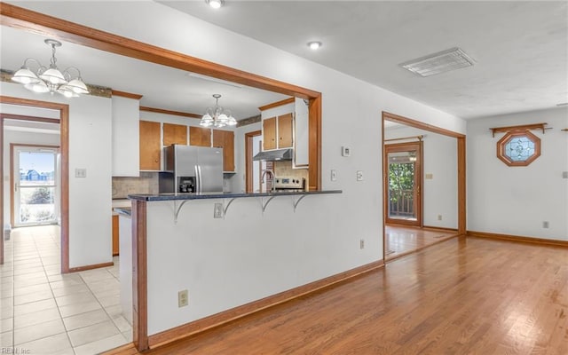 kitchen with decorative light fixtures, a kitchen breakfast bar, a notable chandelier, kitchen peninsula, and stainless steel refrigerator with ice dispenser