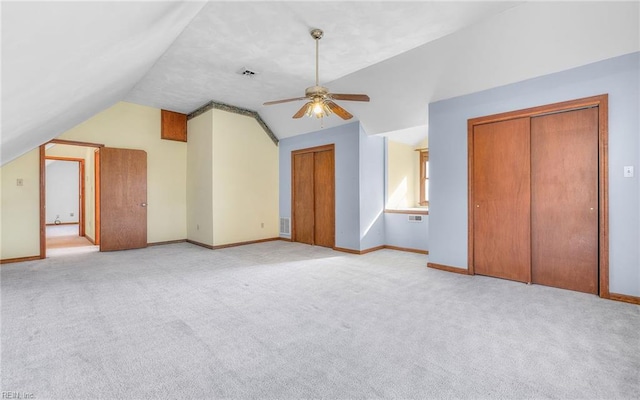 unfurnished bedroom with lofted ceiling, light carpet, and multiple closets