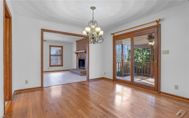 unfurnished living room with ceiling fan with notable chandelier, a fireplace, and light hardwood / wood-style flooring