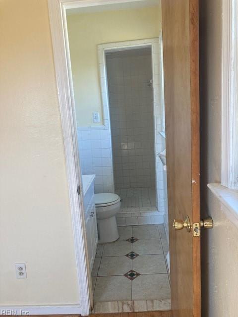 bathroom with tile patterned flooring, vanity, tiled shower, and toilet