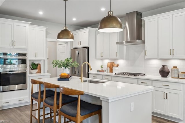 kitchen featuring an island with sink, appliances with stainless steel finishes, sink, and wall chimney exhaust hood