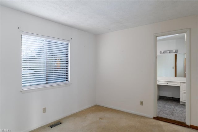 unfurnished bedroom with light colored carpet, a textured ceiling, and ensuite bathroom