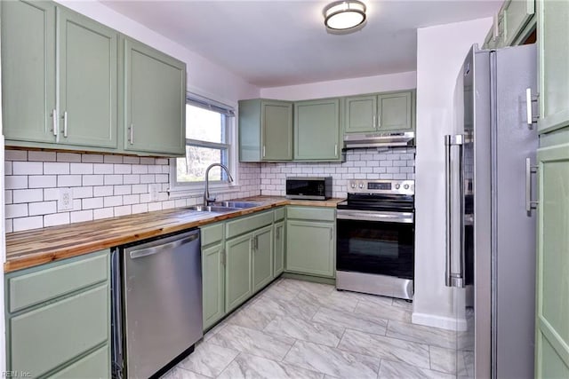 kitchen with wood counters, sink, green cabinetry, appliances with stainless steel finishes, and backsplash