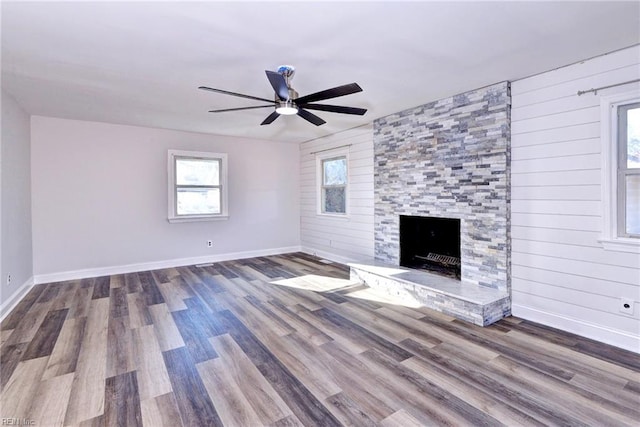 unfurnished living room with wood-type flooring, ceiling fan, a fireplace, and wood walls