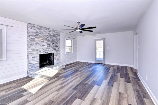 unfurnished living room featuring ceiling fan, wood-type flooring, a fireplace, and wood walls