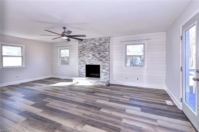 unfurnished living room featuring ceiling fan, a fireplace, plenty of natural light, and dark hardwood / wood-style flooring