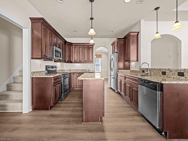 kitchen with appliances with stainless steel finishes, hardwood / wood-style floors, pendant lighting, sink, and kitchen peninsula