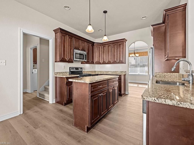 kitchen with sink, light stone counters, hanging light fixtures, stainless steel appliances, and light hardwood / wood-style floors