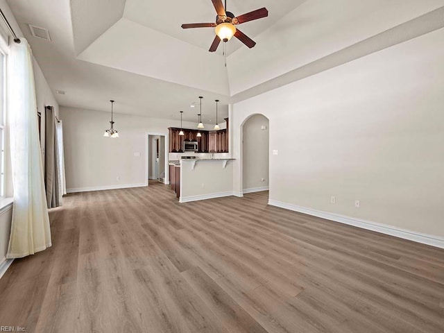 unfurnished living room featuring wood-type flooring, plenty of natural light, a towering ceiling, and ceiling fan