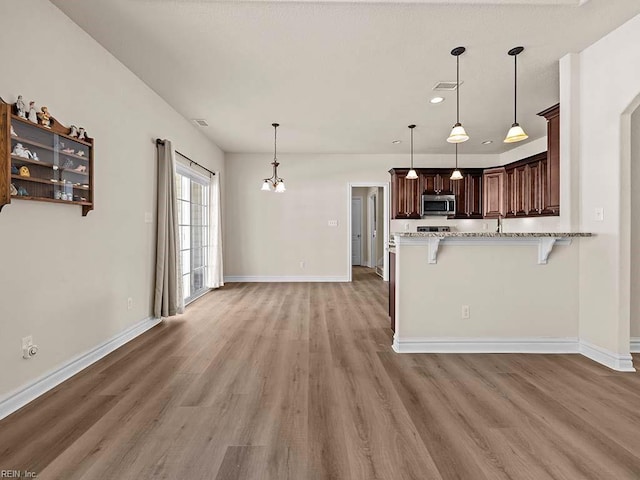 kitchen featuring hanging light fixtures, light stone countertops, a kitchen bar, and kitchen peninsula