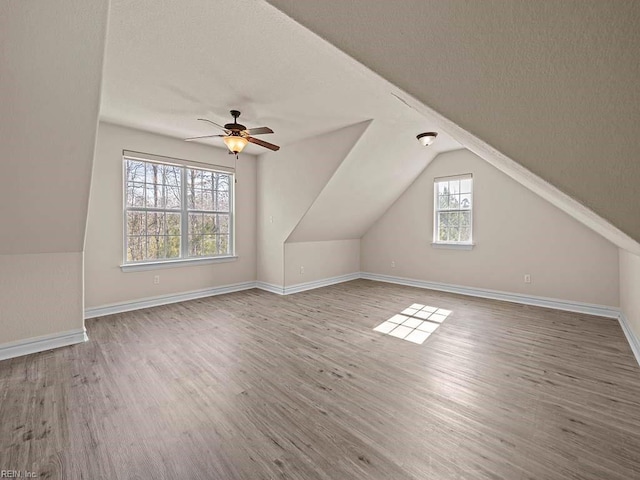 additional living space with hardwood / wood-style flooring, vaulted ceiling, a textured ceiling, and ceiling fan