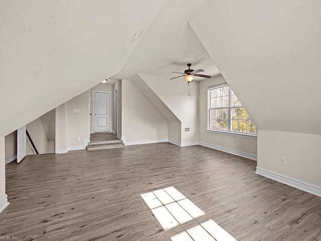 additional living space with vaulted ceiling, a textured ceiling, ceiling fan, and dark hardwood / wood-style flooring