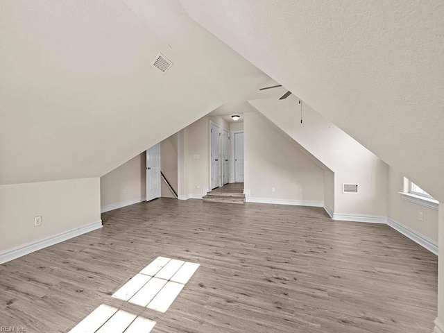 additional living space featuring hardwood / wood-style flooring, lofted ceiling, and a textured ceiling