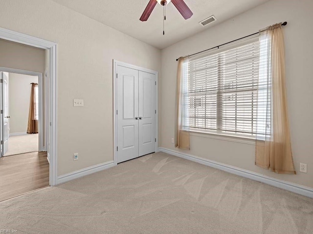 unfurnished bedroom with light carpet, ceiling fan, and a closet