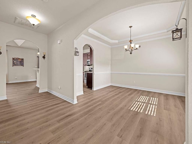 unfurnished room with hardwood / wood-style flooring, ornamental molding, a raised ceiling, and a notable chandelier