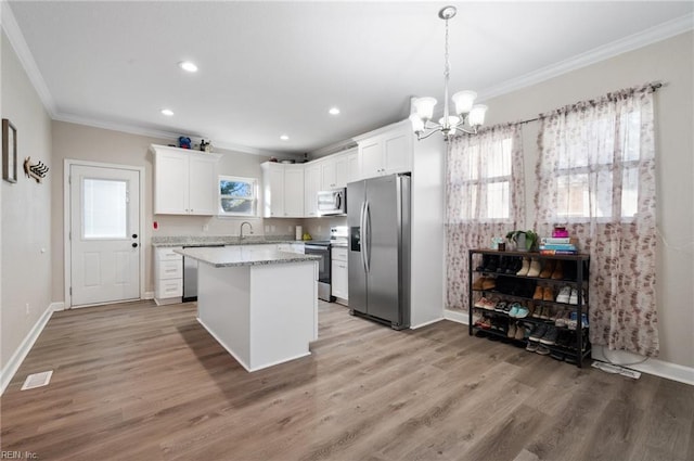 kitchen featuring white cabinetry, ornamental molding, appliances with stainless steel finishes, a kitchen island, and light stone countertops