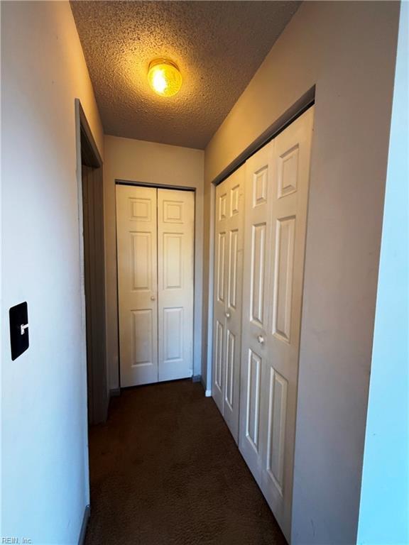 hall with a textured ceiling and dark colored carpet