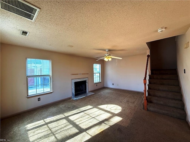 unfurnished living room with ceiling fan, a high end fireplace, carpet floors, and a textured ceiling