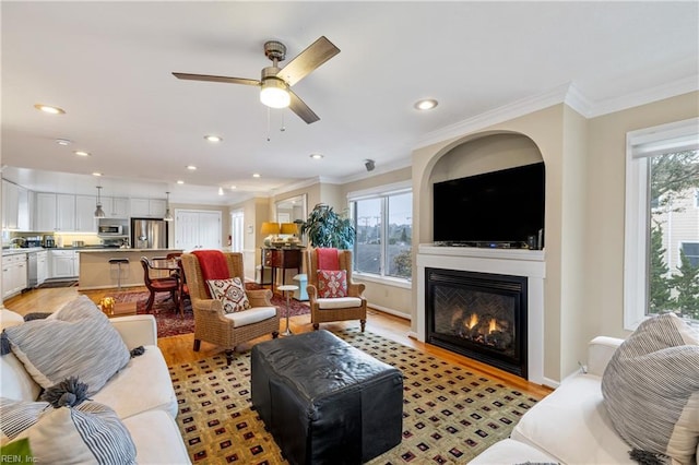 living room featuring ornamental molding, a wealth of natural light, ceiling fan, and light hardwood / wood-style flooring