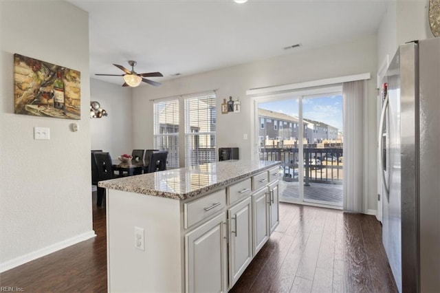 kitchen with dark wood-type flooring, stainless steel refrigerator, light stone counters, white cabinets, and a kitchen island