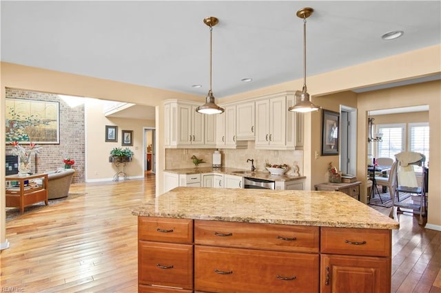 kitchen with decorative light fixtures, decorative backsplash, stainless steel dishwasher, light stone countertops, and light wood-type flooring