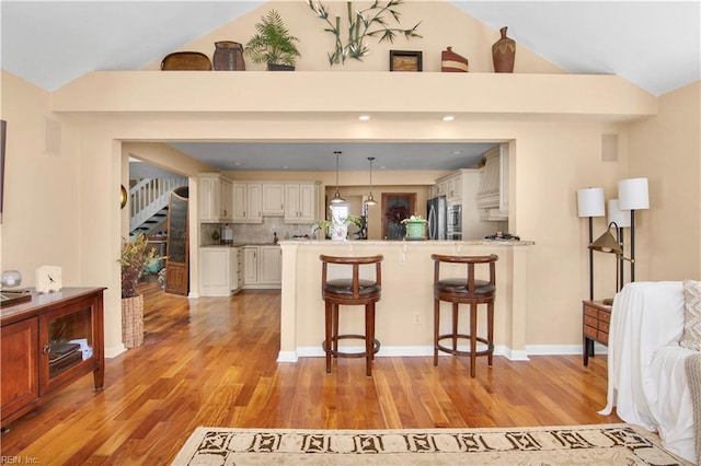 kitchen featuring a breakfast bar, stainless steel refrigerator, decorative backsplash, hanging light fixtures, and kitchen peninsula