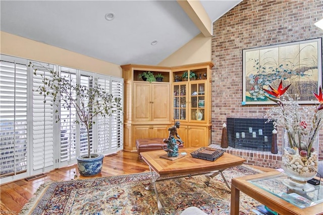 living room featuring vaulted ceiling, a brick fireplace, and light hardwood / wood-style floors