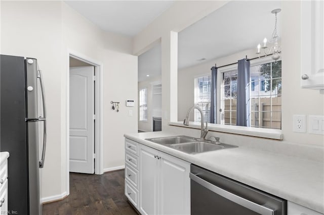 kitchen with appliances with stainless steel finishes, sink, white cabinets, hanging light fixtures, and dark wood-type flooring