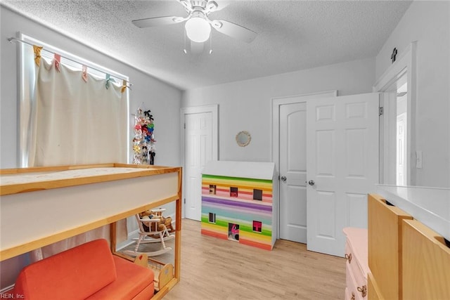 playroom featuring ceiling fan, light hardwood / wood-style flooring, and a textured ceiling