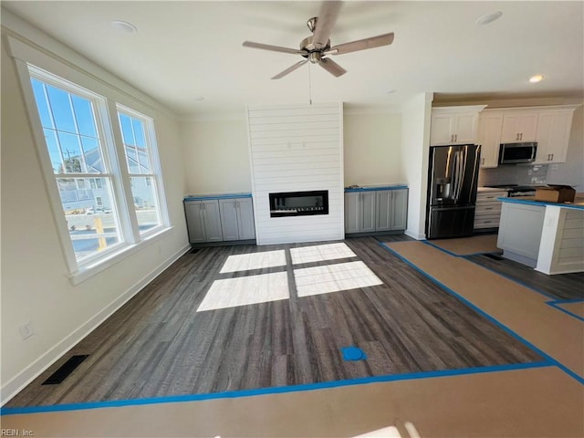 unfurnished living room featuring ornamental molding, ceiling fan, a fireplace, and dark hardwood / wood-style flooring