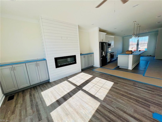 kitchen featuring dark wood-type flooring, range, an island with sink, decorative light fixtures, and black refrigerator with ice dispenser