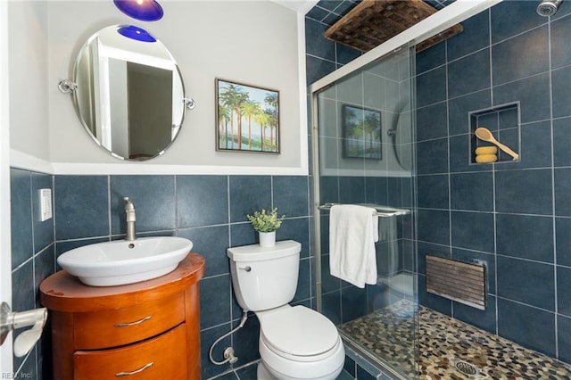 bathroom featuring vanity, toilet, a shower with door, and tile walls