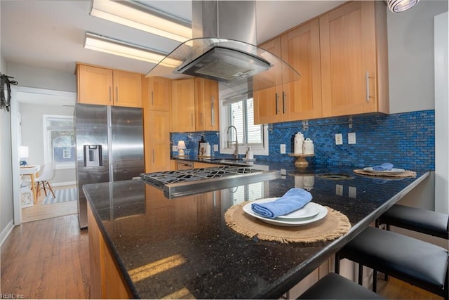 kitchen with sink, island range hood, dark stone countertops, appliances with stainless steel finishes, and backsplash