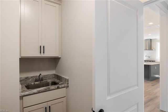 bar featuring light stone countertops, sink, wall chimney range hood, and light hardwood / wood-style floors