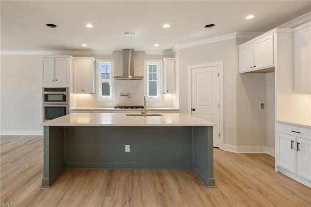 kitchen featuring an island with sink, double oven, and wall chimney exhaust hood