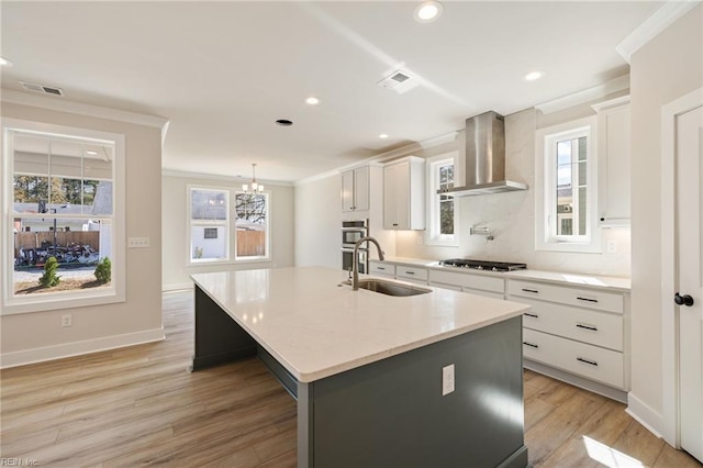 kitchen with sink, a center island with sink, white cabinets, and wall chimney exhaust hood