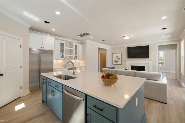 kitchen with sink, a center island with sink, ornamental molding, stainless steel appliances, and white cabinets