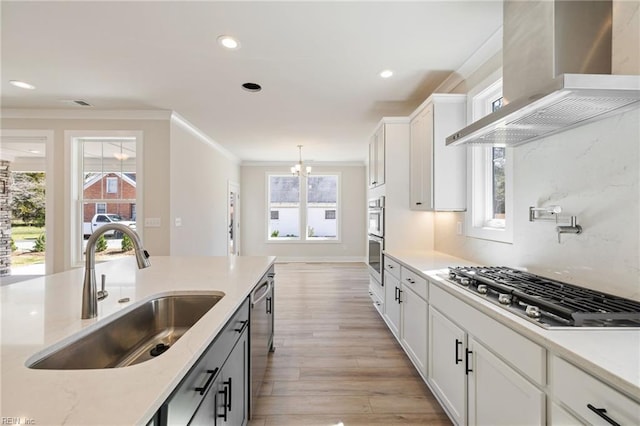 kitchen with decorative light fixtures, white cabinetry, sink, stainless steel appliances, and wall chimney exhaust hood